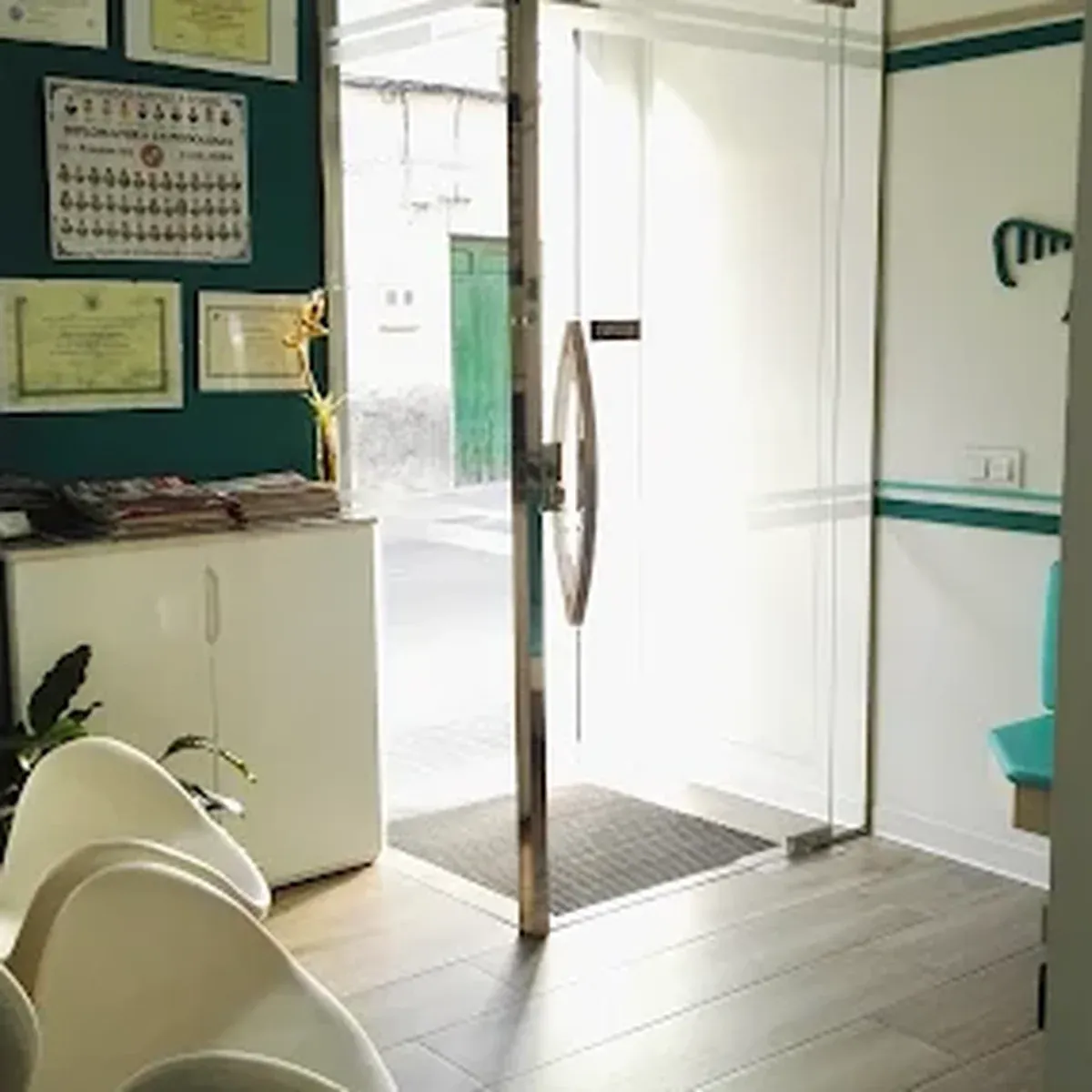 Entrada y mostrador de recepción de la Clínica Podológica Nuria Infantes en Daimiel, con la puerta de cristal y los diplomas en la pared.